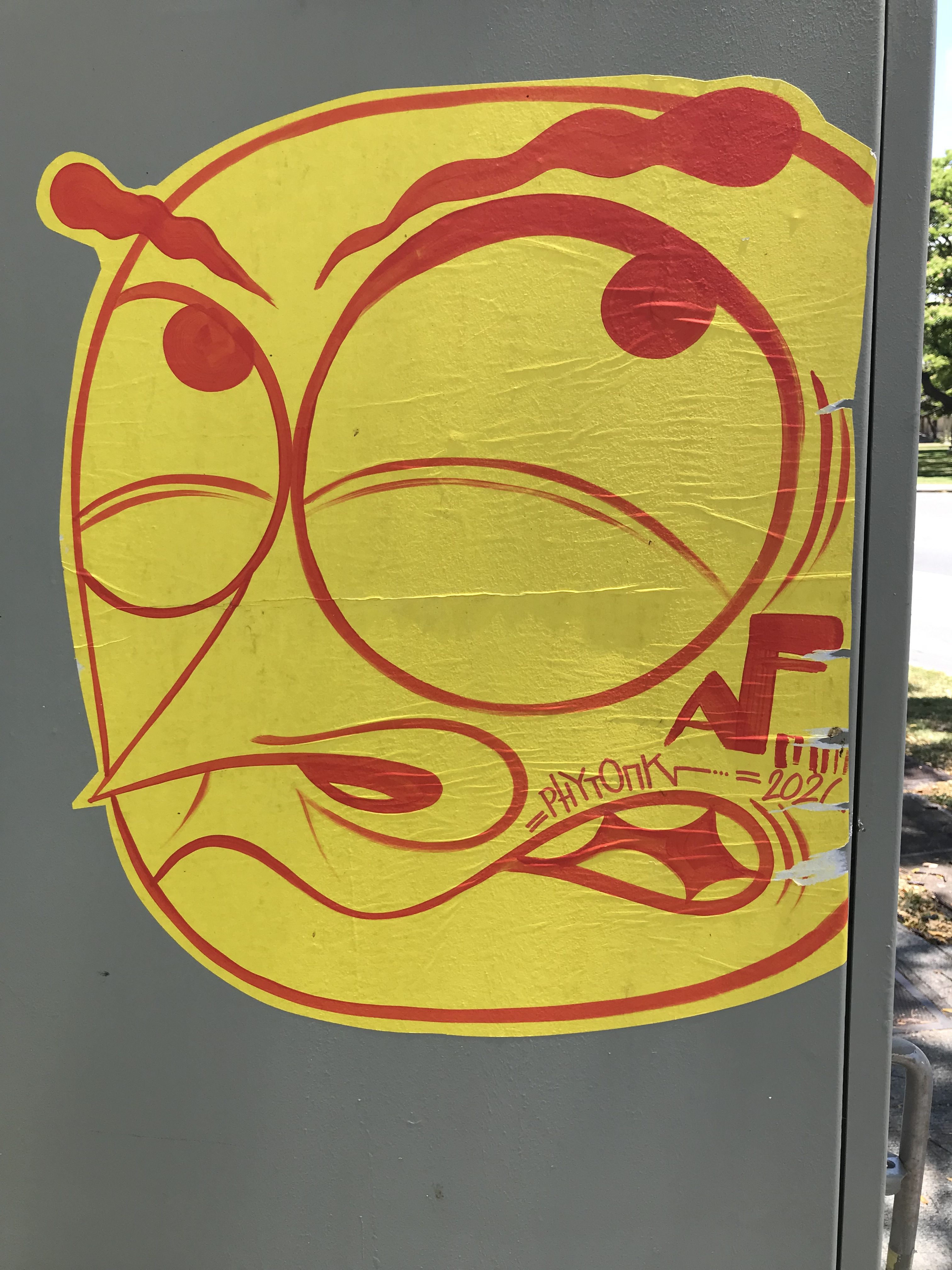 A yellow cartoon-style face with exaggerated features, including large eyes and an expressive mouth, attached to a gray utility box.